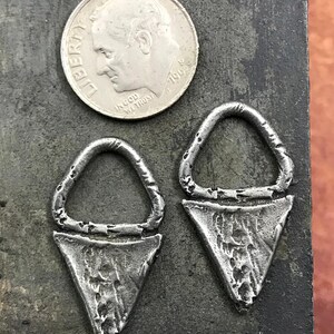 May include: Two silver triangle-shaped earrings with a circular opening at the top. The earrings have a textured, hammered finish.