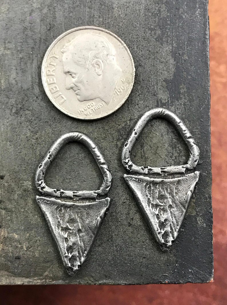 May include: Two silver triangle-shaped earrings with a circular opening at the top. The earrings have a textured, hammered finish.