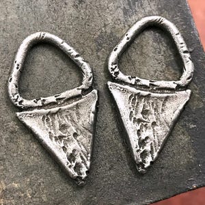 May include: Two silver triangle-shaped earrings with a textured surface and a small loop at the top.