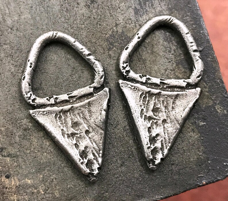 May include: Two silver triangle-shaped earrings with a textured surface and a small loop at the top.