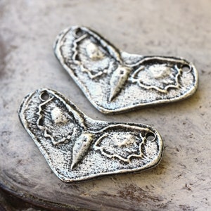 May include: Two silver-toned metal butterfly charms with a detailed, textured design. The charms have a heart shape and a hole at the top for attaching to jewelry or other crafts.