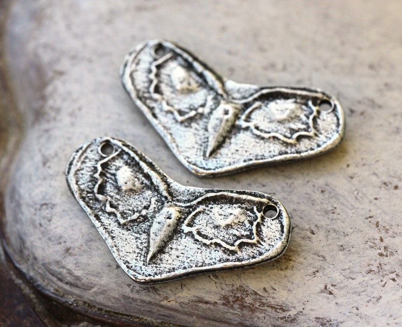 May include: Two silver-toned metal butterfly charms with a detailed, textured design. The charms have a heart shape and a hole at the top for attaching to jewelry or other crafts.