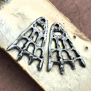 May include: Two silver-toned metal charms shaped like a web or spider web. The charms have a textured, slightly rough surface and are designed to be used for jewelry making.