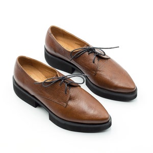 K&ouml;nnte beinhalten: Ein Paar braune Lederschn&uuml;rschuhe mit spitzer Zehenpartie und einer dicken schwarzen Plateau-Sohle.