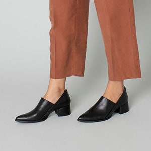 May include: Black leather heeled shoes with a pointed toe and a cut-out detail on the side. The shoes have a block heel.