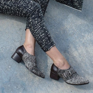 May include: A pair of black and white patterned pants with a black jacket. The person is wearing black and white shoes with a brown heel.