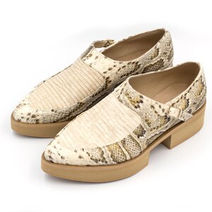 Puede incluir: Un par de zapatos de piel de serpiente beige y marr&oacute;n con una correa de hebilla y una suela de plataforma gruesa.