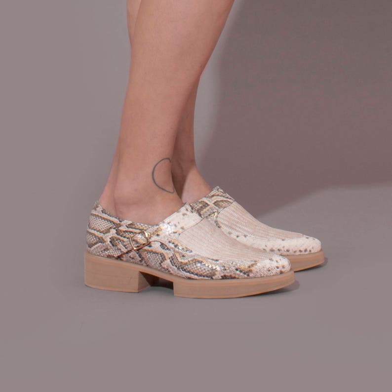 Puede incluir: Zapatos de plataforma beige con estampado de piel de serpiente y una correa con hebilla. Los zapatos tienen un tac&oacute;n grueso y una punta puntiaguda.