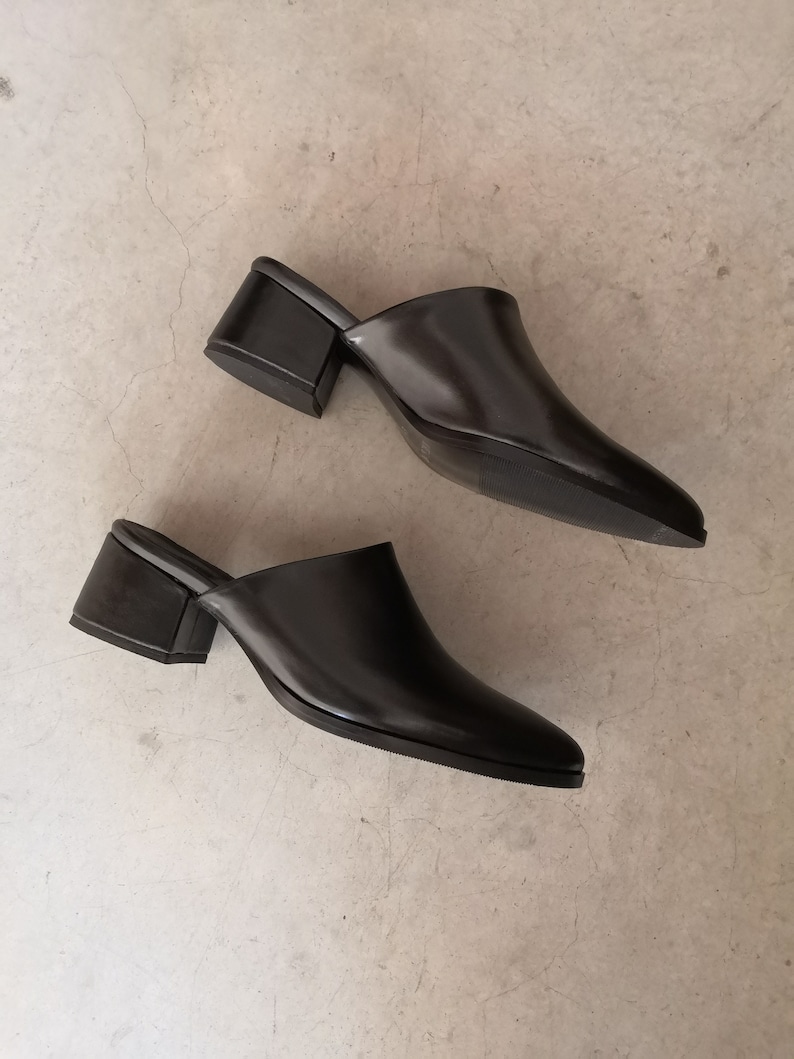 May include: A pair of black leather mules with a square block heel. The shoes have a pointed toe and a slip-on design. The heels are approximately 2 inches high.