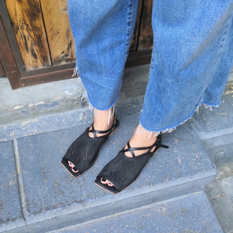 May include: A pair of black mesh sandals with criss-cross straps. The sandals have a square toe and a low heel.