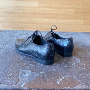 May include: A pair of black leather shoes with a crocodile pattern. The shoes have laces and a pointed toe.