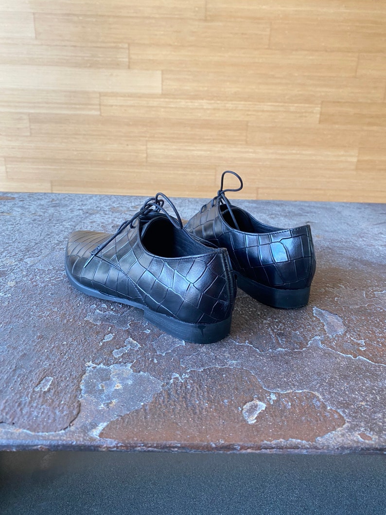 May include: A pair of black leather shoes with a crocodile pattern. The shoes have laces and a pointed toe.
