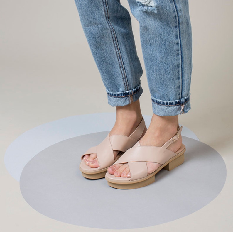 K&ouml;nnte beinhalten: Ein Paar hellrosa Ledersandalen mit einem Kreuzriemen-Design und einem dicken Absatz.