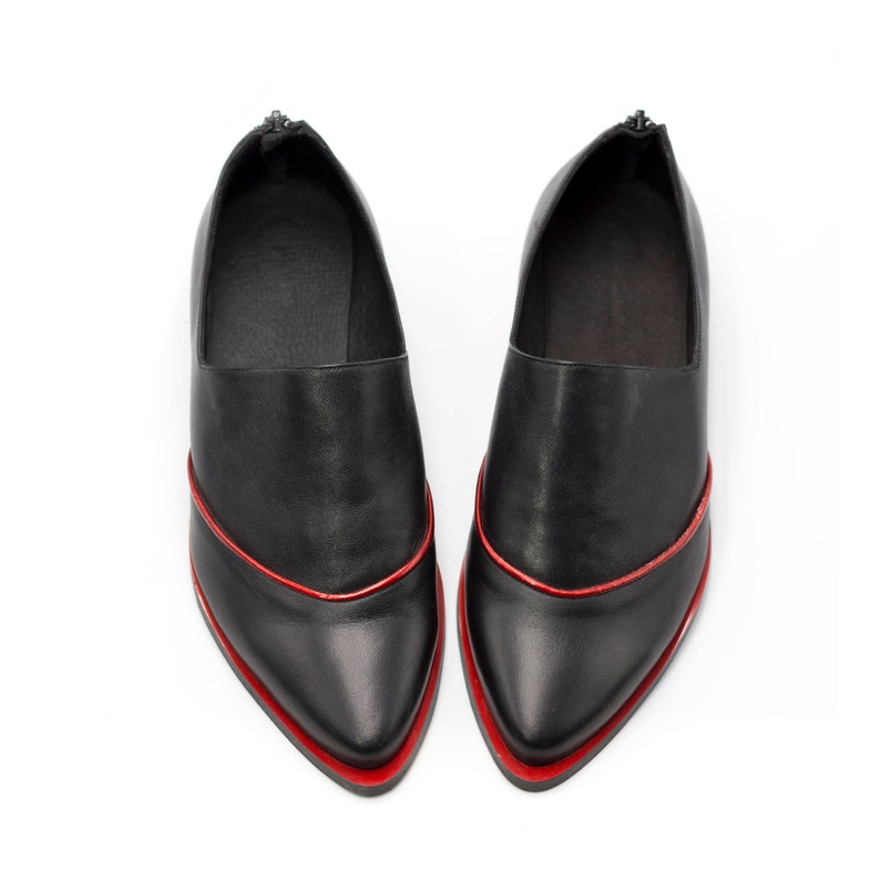Puede incluir: Un par de zapatos de cuero negro con punta puntiaguda y un borde rojo.