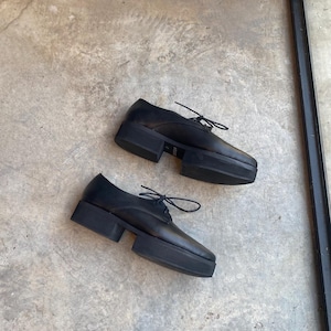 May include: A pair of black leather platform shoes with lace-up fastenings. The shoes have a chunky platform sole and a rounded toe.