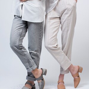 May include: Two people wearing casual clothing and gray and tan heeled mules. The person on the left is wearing gray jeans and a white button-down shirt. The person on the right is wearing white pants and a white t-shirt.