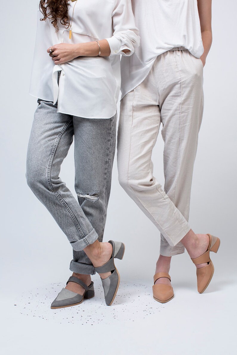 May include: Two people wearing casual clothing and gray and tan heeled mules. The person on the left is wearing gray jeans and a white button-down shirt. The person on the right is wearing white pants and a white t-shirt.