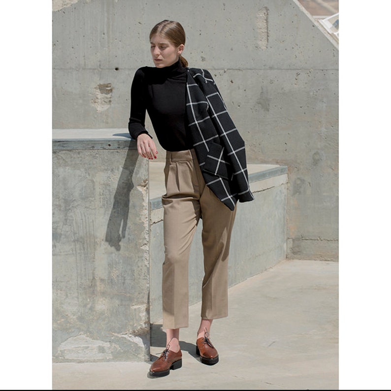 K&ouml;nnte beinhalten: Eine Frau tr&auml;gt einen schwarzen Rollkragenpullover, eine beige Hose und braune Lederschn&uuml;rschuhe. Sie tr&auml;gt einen schwarz-wei&szlig; karierten Blazer &uuml;ber ihrem Pullover.