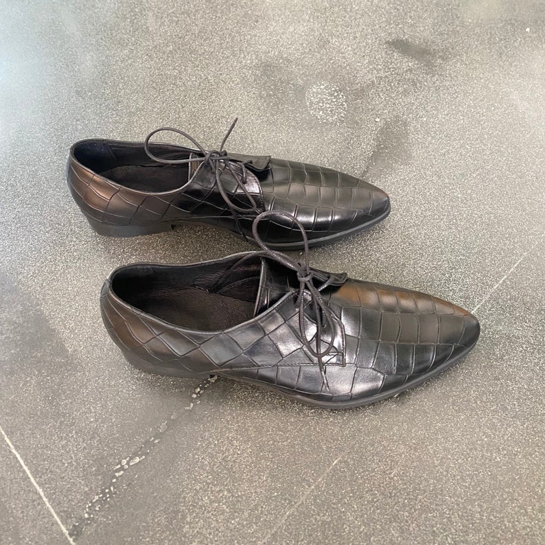 May include: A pair of black leather shoes with a crocodile pattern. The shoes have laces and a pointed toe.