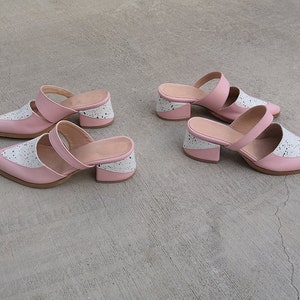 May include: Two pairs of pink and white heeled mules with a chunky heel. The shoes have a two-strap design and a pointed toe.
