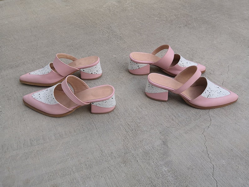 May include: Two pairs of pink and white heeled mules with a chunky heel. The shoes have a two-strap design and a pointed toe.