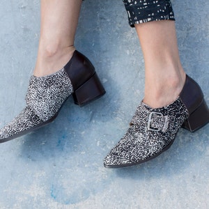 May include: A pair of black and white heeled shoes with a buckle detail. The shoes have a pointed toe and a block heel.