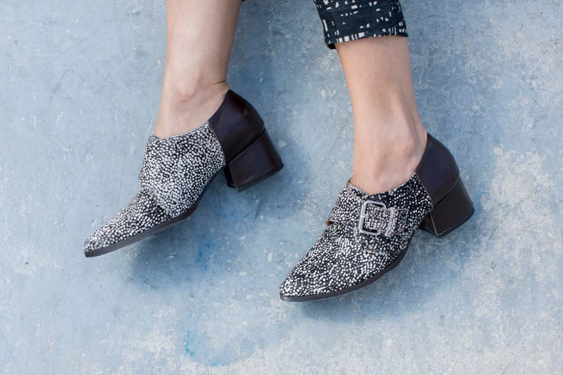 May include: A pair of black and white heeled shoes with a buckle detail. The shoes have a pointed toe and a block heel.