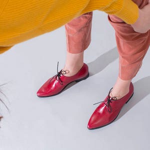 May include: A pair of red leather oxfords with black laces. The shoes have a pointed toe and a low heel.