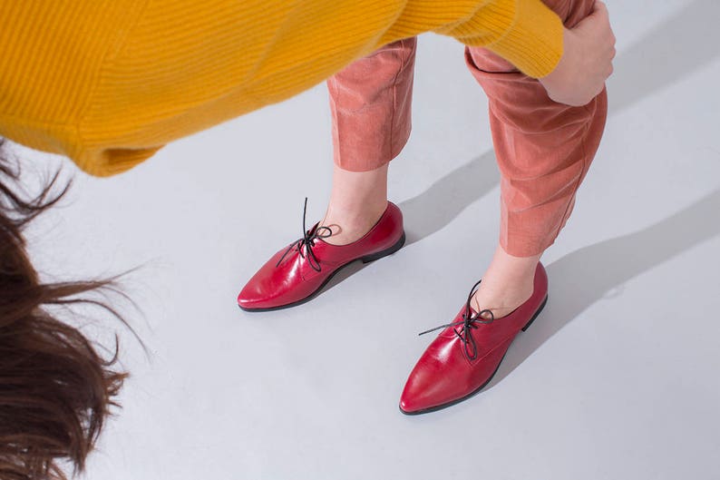 May include: A pair of red leather oxfords with black laces. The shoes have a pointed toe and a low heel.