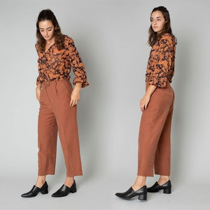 May include: Two women wearing a brown and black floral print blouse with long sleeves and rust colored cropped pants. Both women are wearing black heeled shoes.