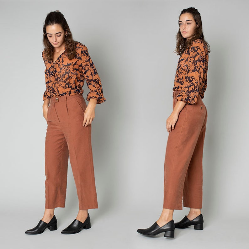 May include: Two women wearing a brown and black floral print blouse with long sleeves and rust colored cropped pants. Both women are wearing black heeled shoes.