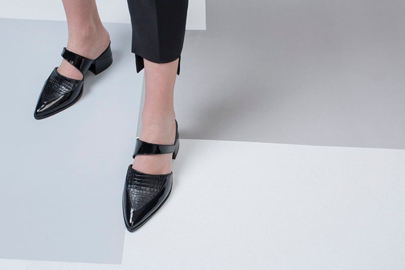 Puede incluir: Un par de zapatos de tac&oacute;n de cuero negro con punta puntiaguda y una tira sobre la parte superior del pie.