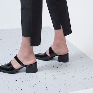 May include: Black heeled mules with a pointed toe and two straps. The shoes have a textured, crocodile-embossed design.