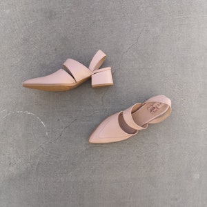 May include: A pair of light pink heeled shoes with a pointed toe and a strap across the top of the foot. The shoes have a small block heel.