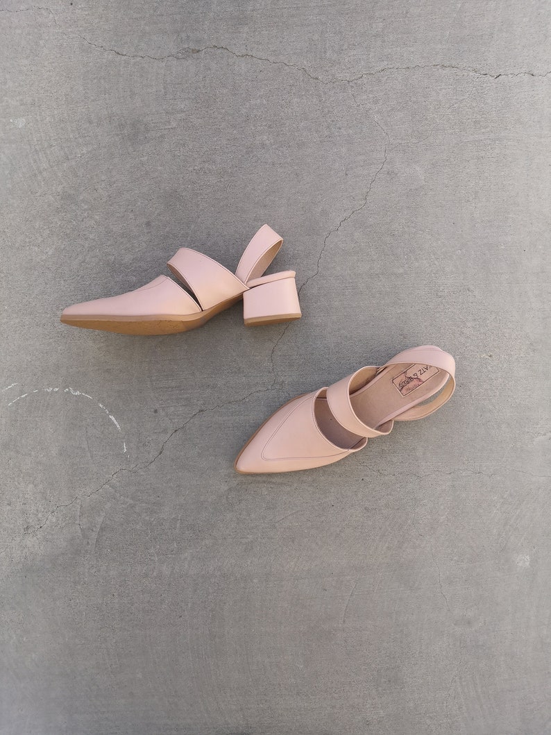 May include: A pair of light pink heeled shoes with a pointed toe and a strap across the top of the foot. The shoes have a small block heel.