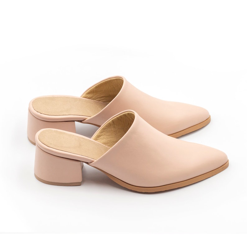 May include: A pair of blush pink heeled mules with a pointed toe and a block heel.