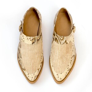 Puede incluir: Un par de zapatos de punta beige con estampado de piel de serpiente y cierre de hebilla.