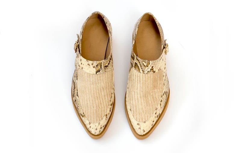 Puede incluir: Un par de zapatos de punta beige con estampado de piel de serpiente y cierre de hebilla.