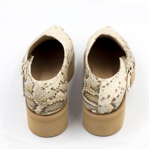 Puede incluir: Un par de zapatos de piel de serpiente con estampado beige y marr&oacute;n, con un tac&oacute;n grueso y cierre de hebilla.