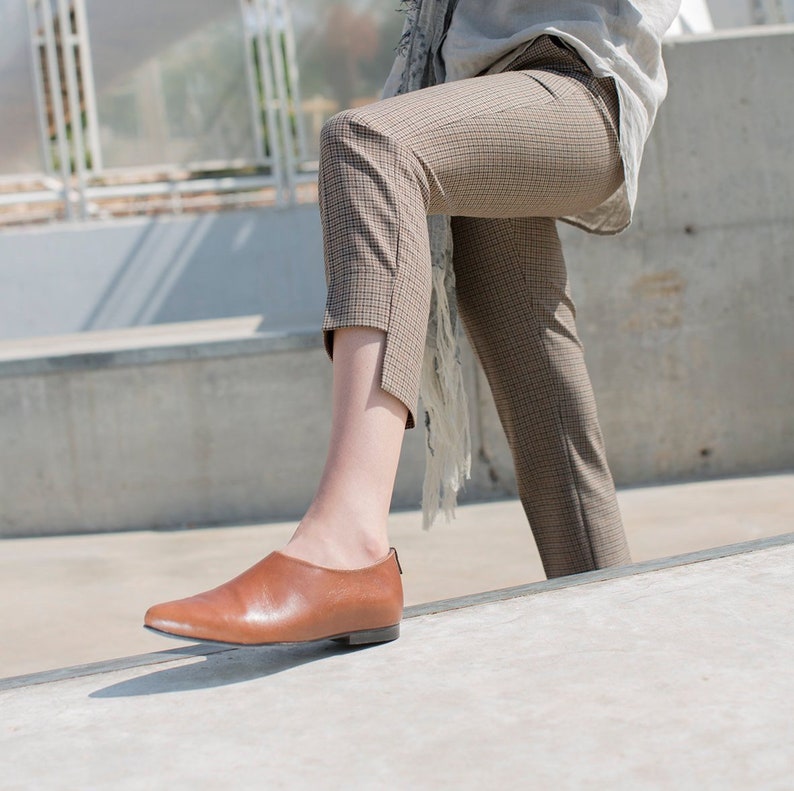 May include: A person wearing brown checkered pants and brown leather slip-on shoes.