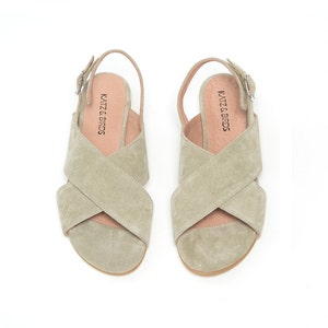 K&ouml;nnte beinhalten: Ein Paar hellgr&uuml;ne Wildledersandalen mit einem Kreuzriemen-Design und einem Schnallenverschluss. Die Sandalen haben ein "KATZ & BIRDS"-Etikett auf der Innensohle.