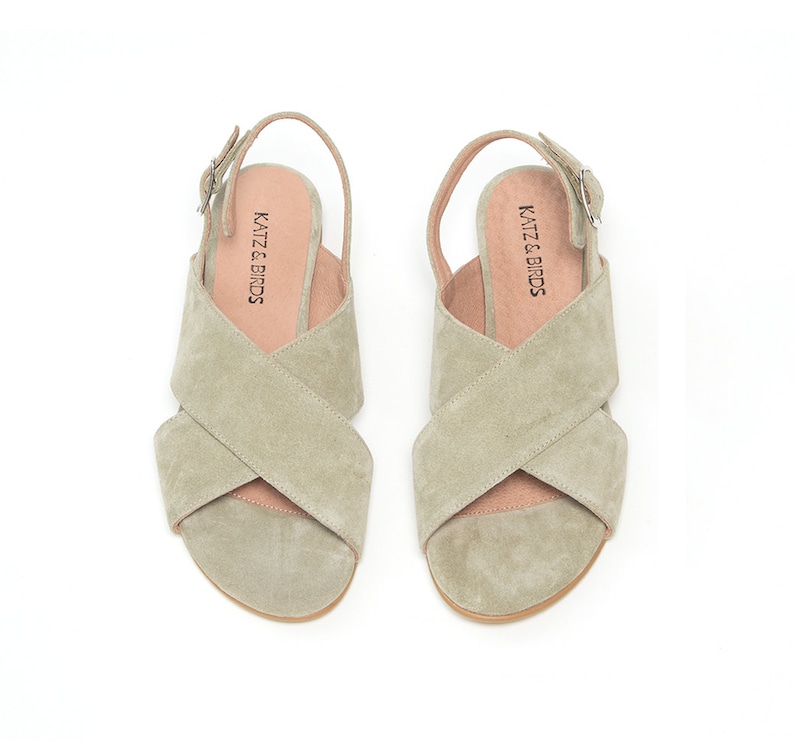 K&ouml;nnte beinhalten: Ein Paar hellgr&uuml;ne Wildledersandalen mit einem Kreuzriemen-Design und einem Schnallenverschluss. Die Sandalen haben ein "KATZ & BIRDS"-Etikett auf der Innensohle.