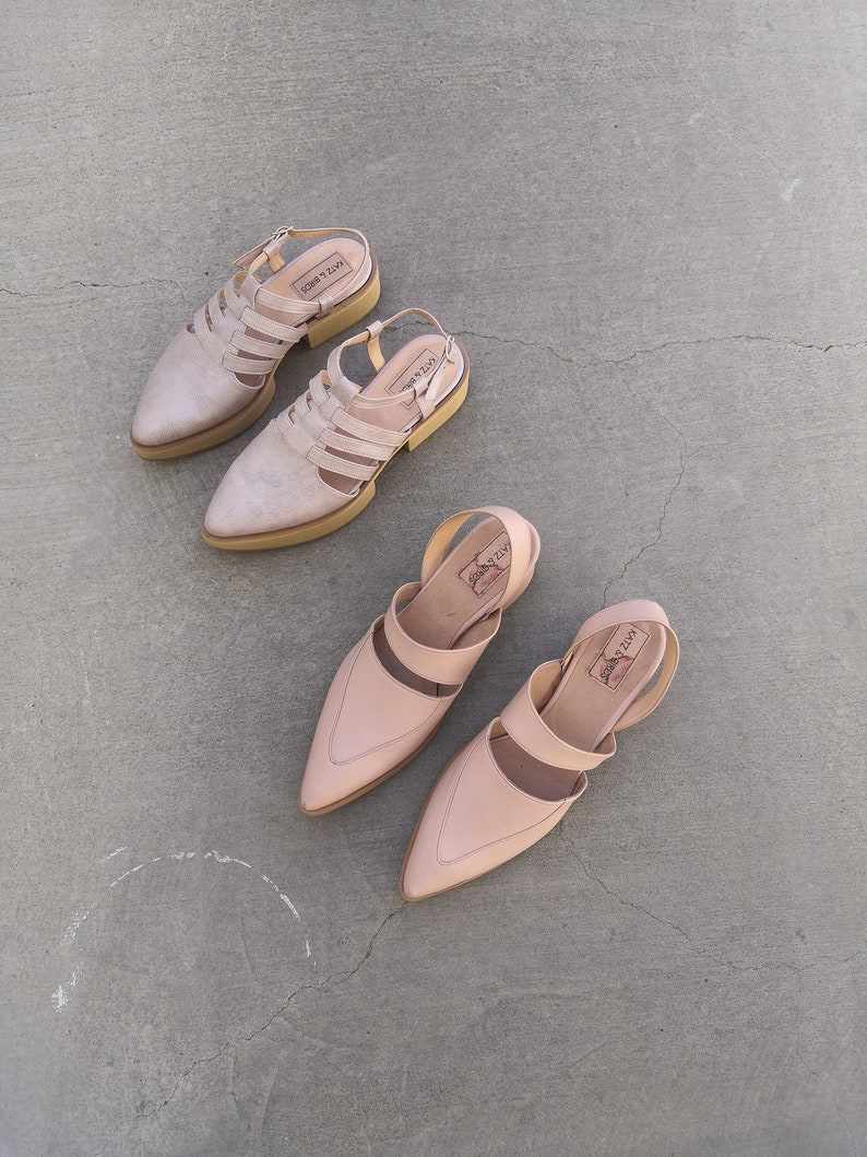 May include: Three pairs of light pink leather sandals with ankle straps. The sandals have a pointed toe and a low heel. The brand name "LAZY" is visible on the straps.