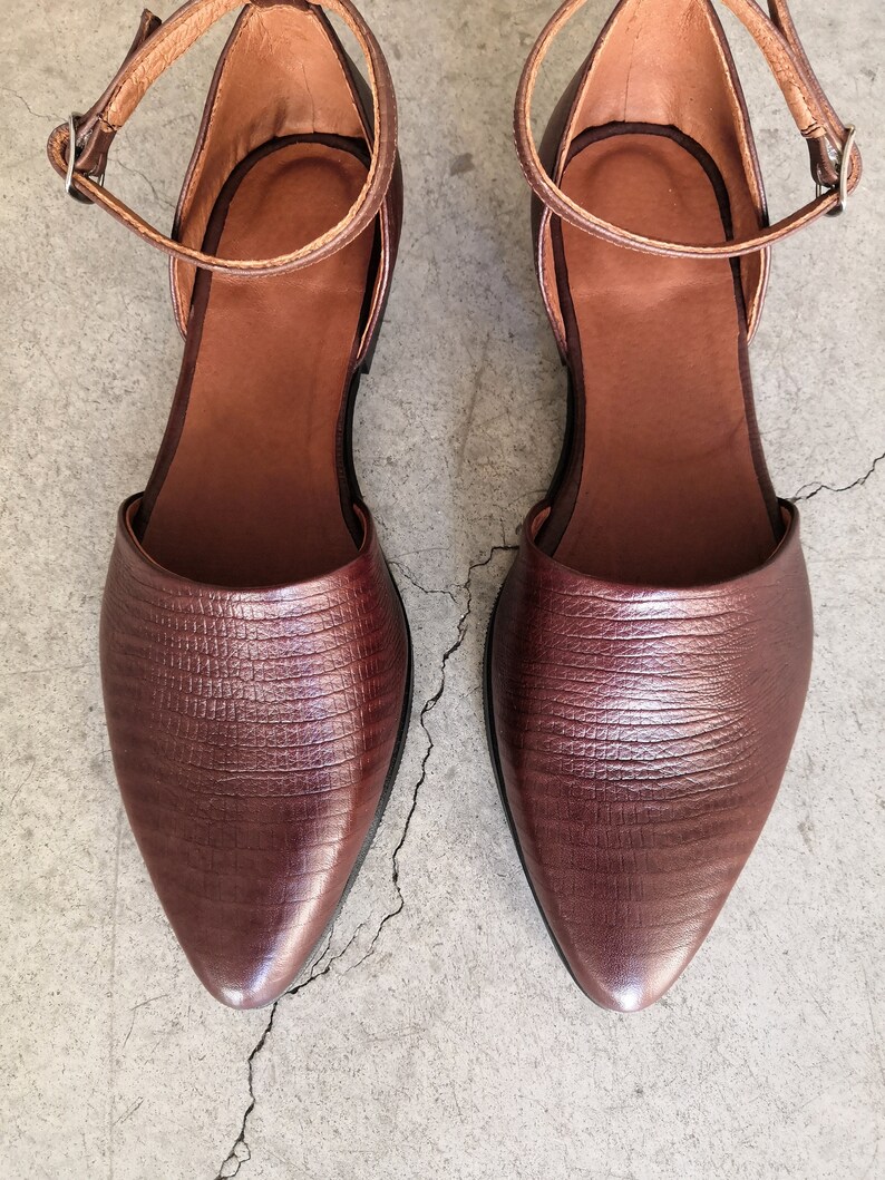 May include: A pair of brown leather ankle strap sandals with pointed toes. The sandals feature a textured leather upper and a simple ankle strap with a buckle fastening.