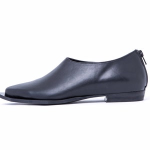 May include: Black leather slip-on shoe with a pointed toe and a zipper on the back.