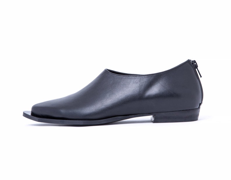 May include: Black leather slip-on shoe with a pointed toe and a zipper on the back.