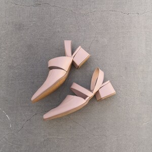 May include: A pair of light pink heeled sandals with a cut-out design. The sandals have a block heel and an ankle strap.