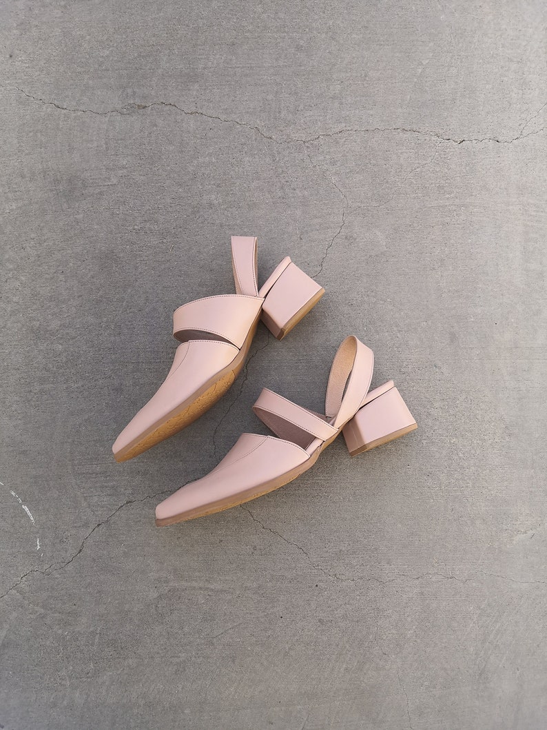 May include: A pair of light pink heeled sandals with a cut-out design. The sandals have a block heel and an ankle strap.