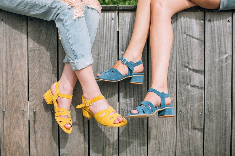 May include: Two people wearing sandals with contrasting colors. One person is wearing yellow sandals and the other is wearing blue sandals. Both sandals have a strap across the ankle and a thick heel.