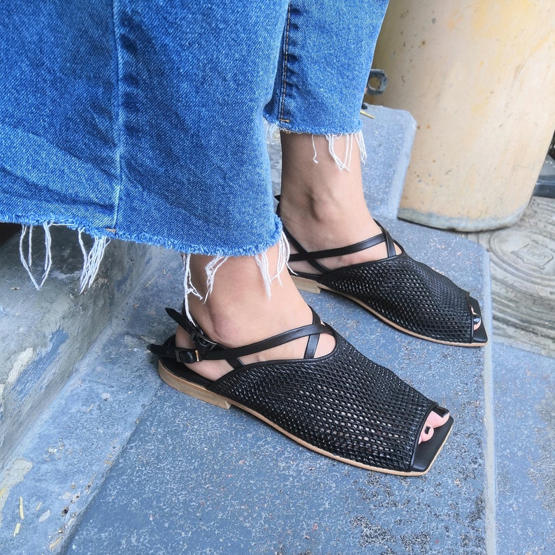 May include: A pair of black woven sandals with a criss-cross strap design and a peep-toe style.